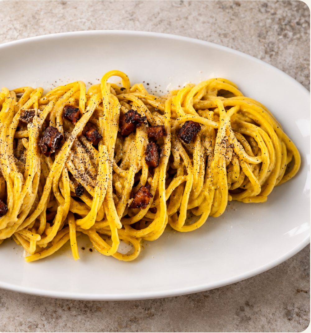 Spaghetti alla carbonara vegana con crema gialla, pepe nero e cubetti di seitan glassato